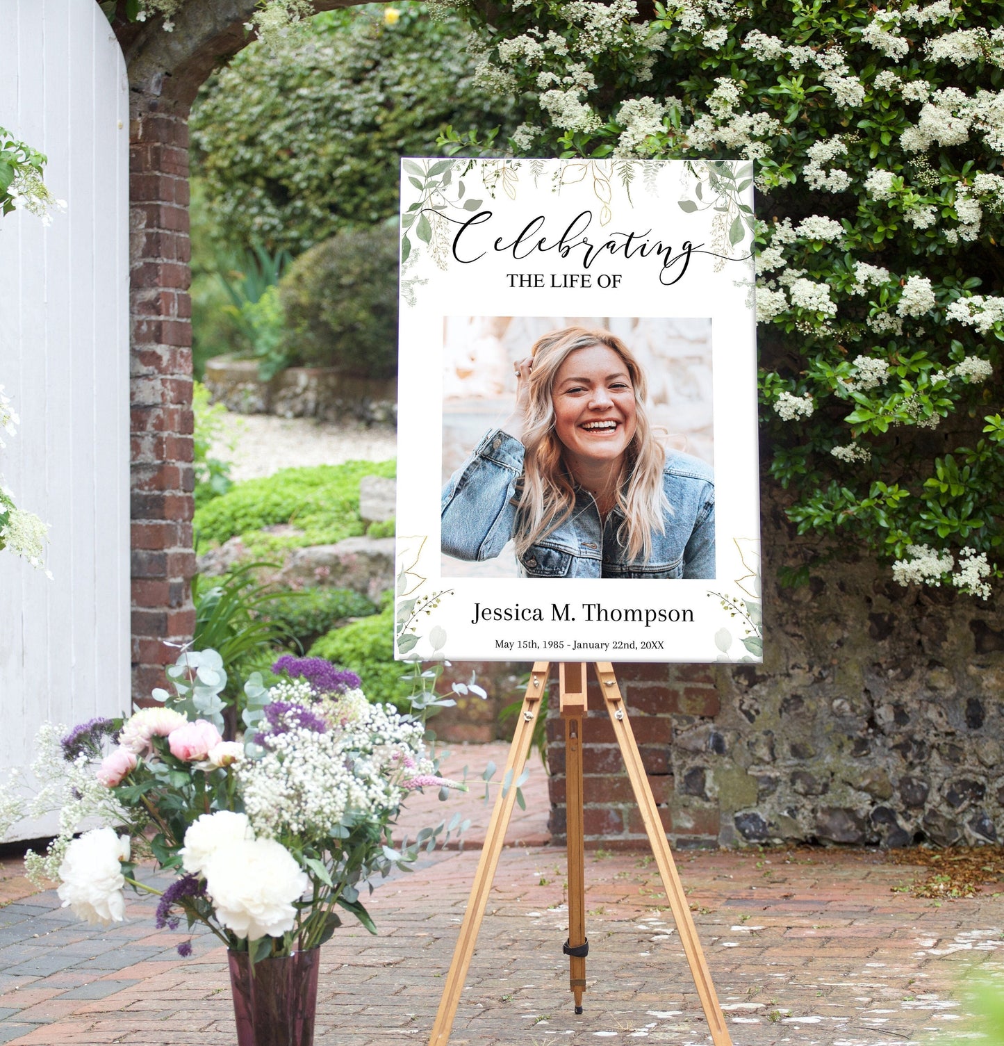 A funeral poster sits on an easel, it has a leafy green background with celebrating the life of written above the center photo. 